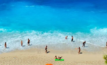 Aerial view of a tropical beach with colorful umbrellas and people swimming in turquoise water.