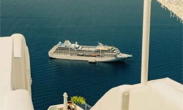 Cruise ship sailing near Santorini with white cliffside architecture overlooking the Aegean Sea