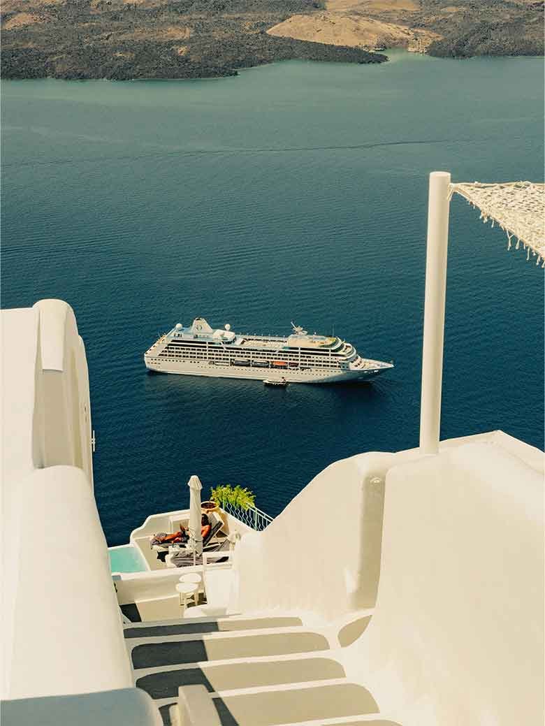 Cruise ship sailing near Santorini with white cliffside architecture overlooking the Aegean Sea